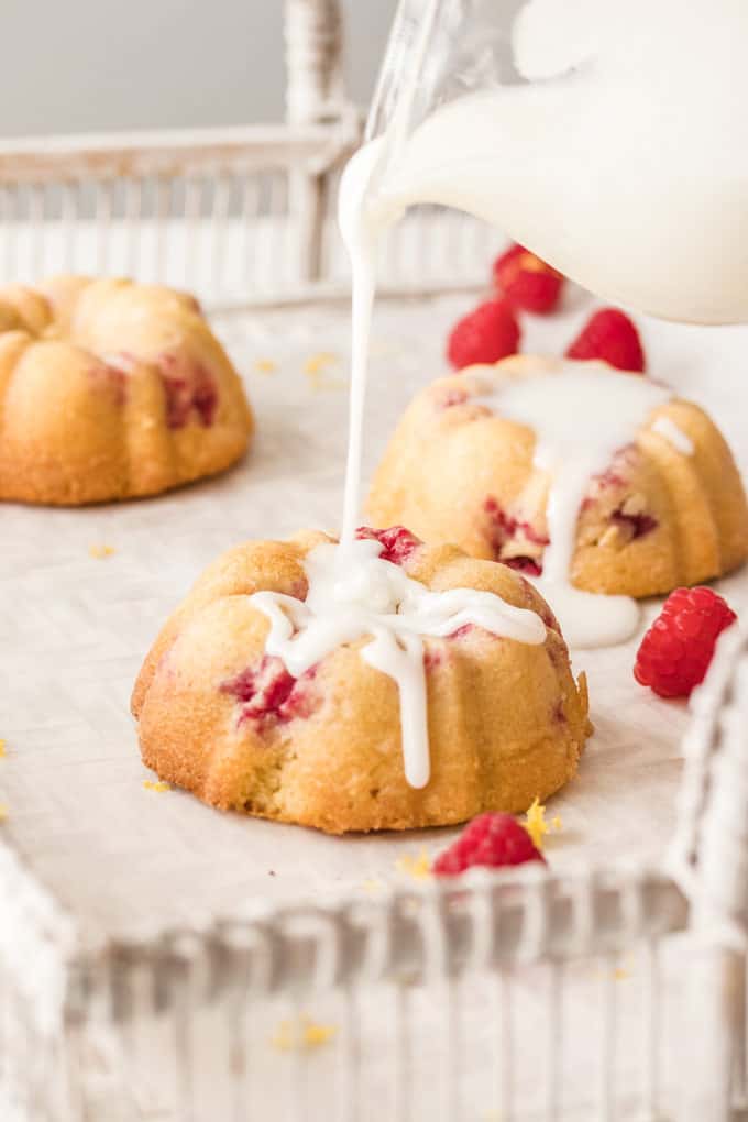 Icing drizzling on a mini bundt cake, raspberries strewn about