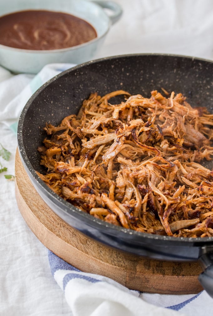 A frying pan filled with shredded pork with bbq sauce in the background
