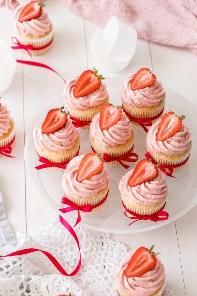 Top down view of a plate of 7 vanilla cupcakes with strawberry buttercream