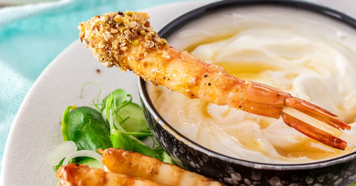 A dukkah crust prawn sitting on top of a bowl of yoghurt.
