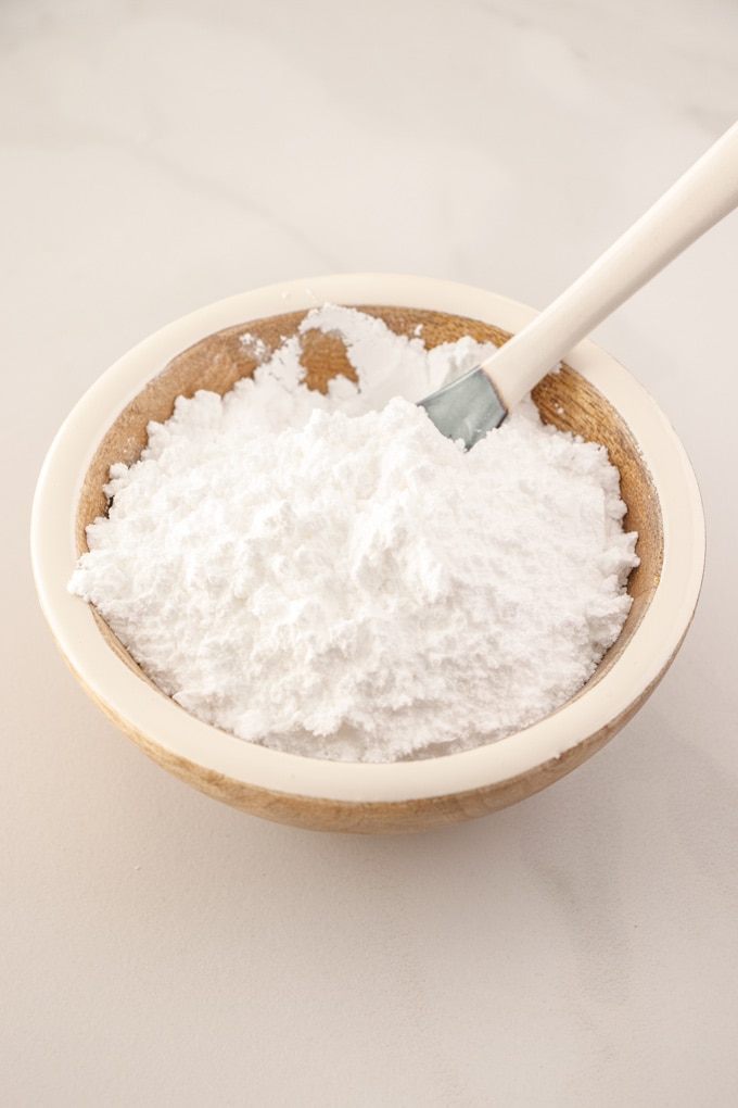 A wooden bowl of icing sugar with a spoon sticking out