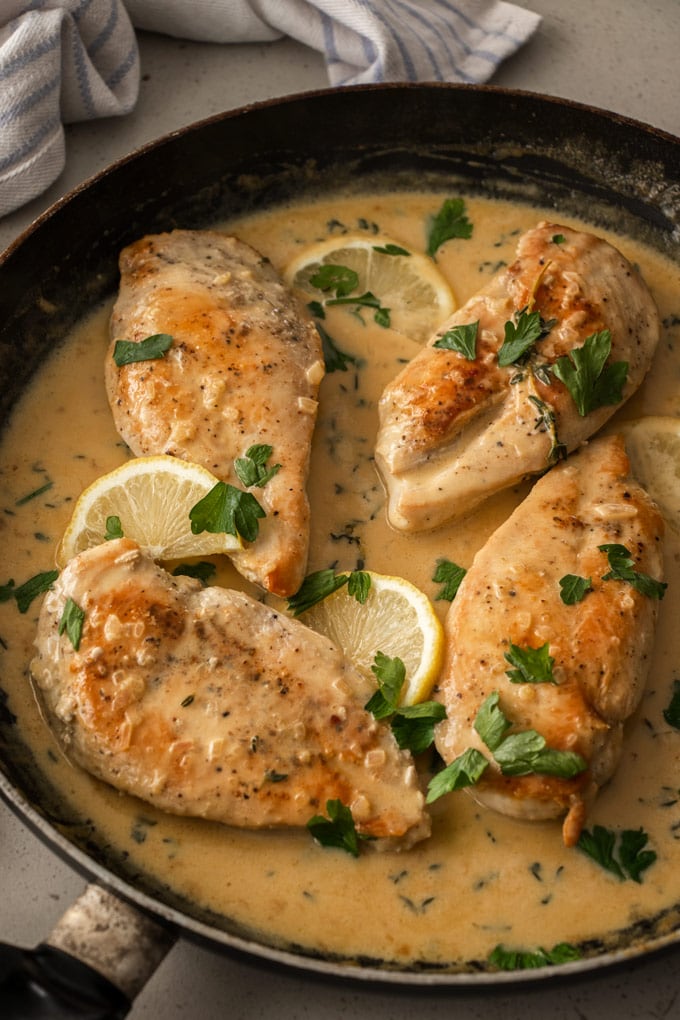 A pan with 4 cooked chicken breasts in a creamy sauce