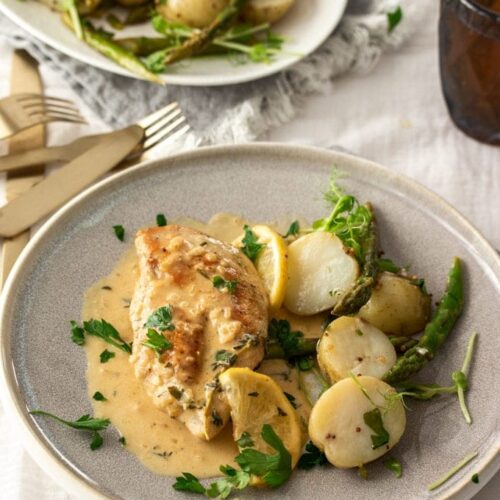 A grey plate with a chicken breast, potatoes and a cream sauce