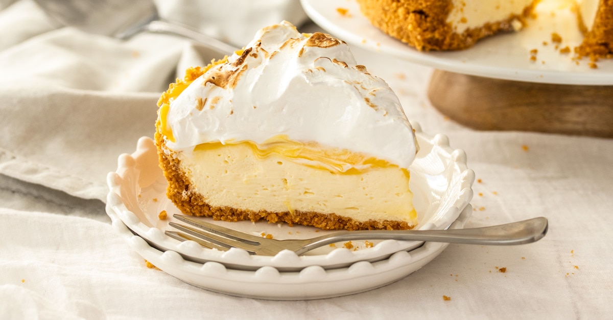 A close up of a slice of lemon meringue cheesecake on a white plate with a fork next to it