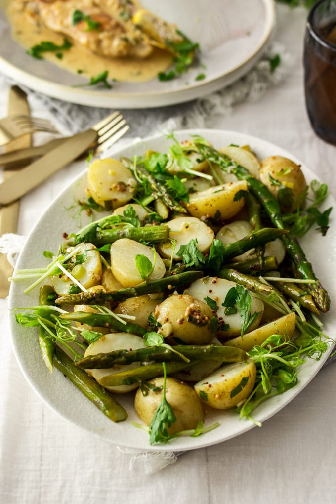Potato asparagus salad on a white plate with gold cutlery