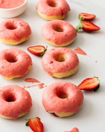 7 baked doughnuts with pink frosting surrounded by strawberries