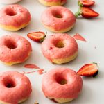 Two rows of 3 doughnuts with pink icing surrounded by cut strawberries