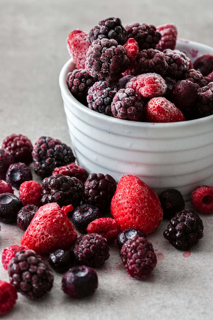 A whlte bowl overflowing with mixed frozen berries on a grey background
