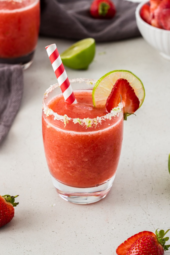 A single glass of frozen strawberry daiquiri with a slice of lime and strawberry