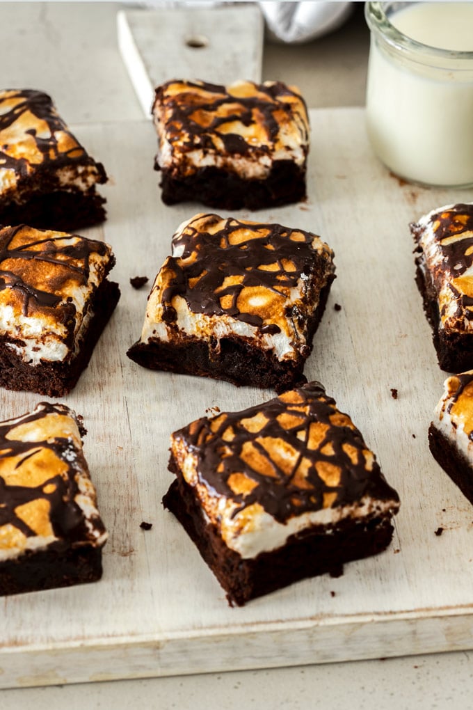 A row of 3 Fudgy Marshmallow Brownies in the middle with a glass of milk in the background off to the side