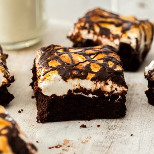 A closeup of a marshmallow topped chocolate brownie with a glass of milk in the background