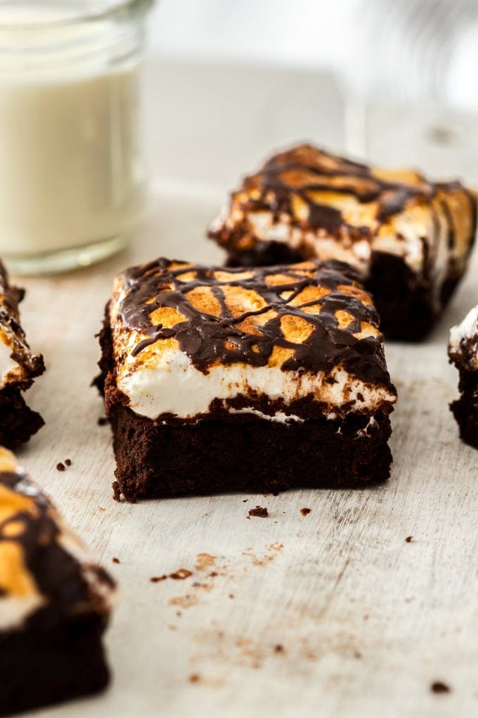 A closeup of a marshmallow topped chocolate brownie with a glass of milk in the background