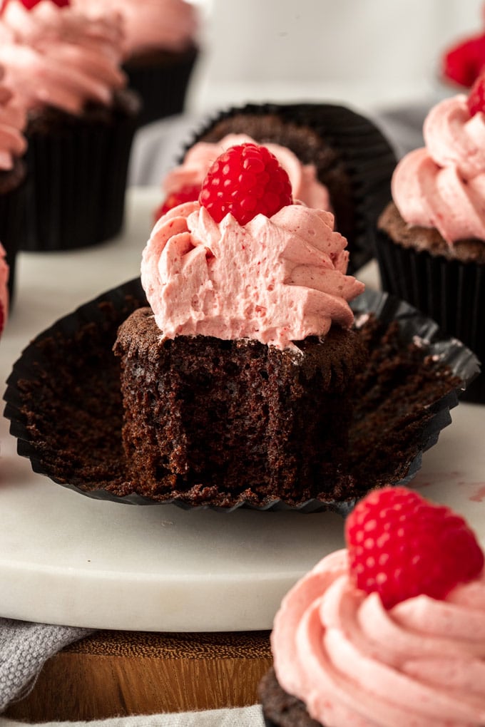 A chocolate cupcake with raspberry frosting with a bite taken out of it.