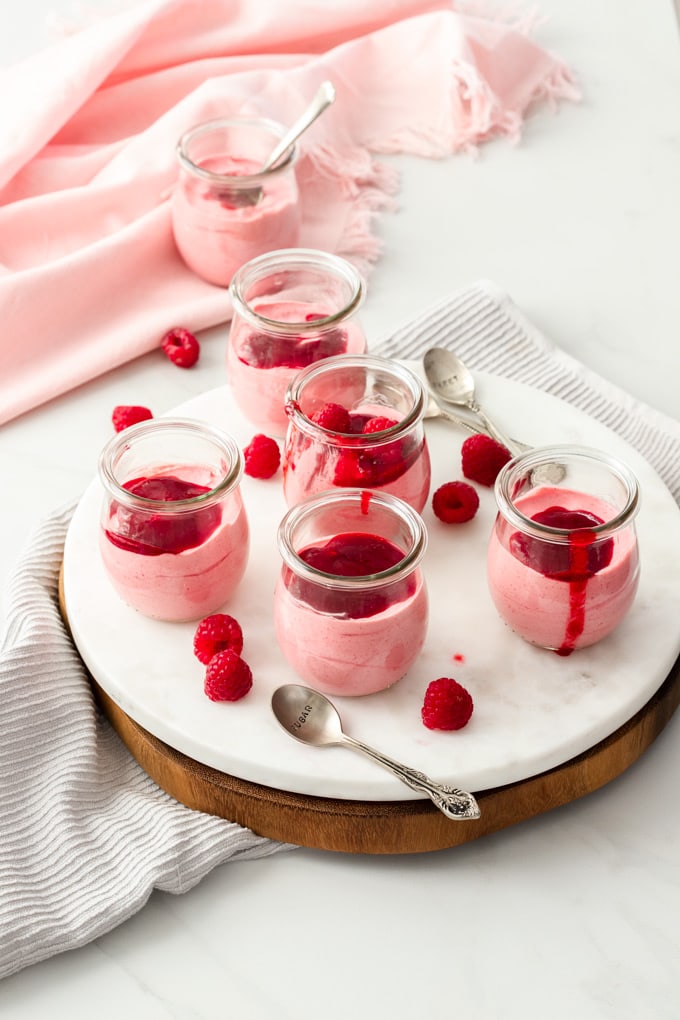 5 small glass pots of pink mousse sitting on a white marble platter