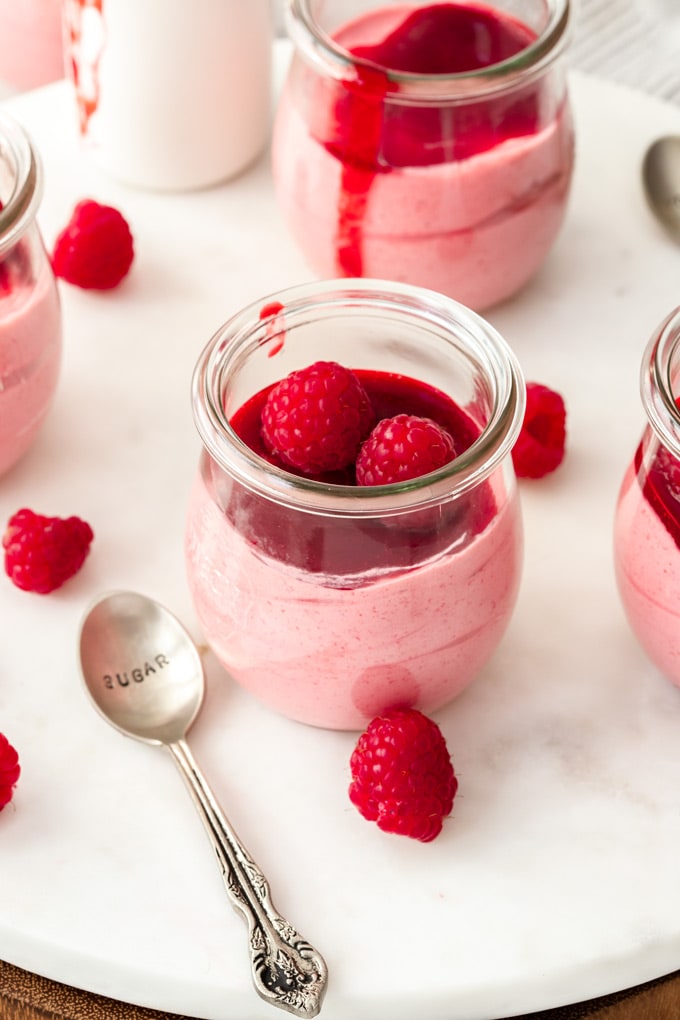 A small glass jar filled with pink raspberry mousse and fresh raspberries