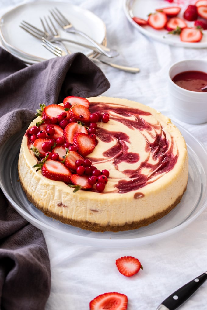 A strawberry swirl cheesecake decorated with fresh strawberries and red currants