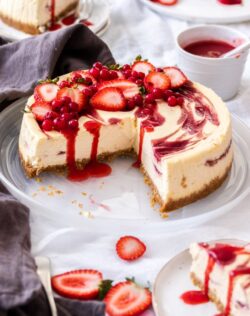 A strawberry swirl cheesecake with a quarter of it sliced away, on a white plate