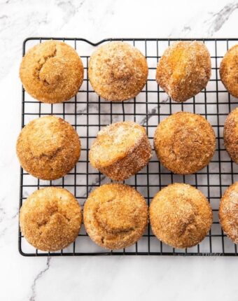 A batch of cinnamon sugar muffins on a black cooling rack on a marble surface.
