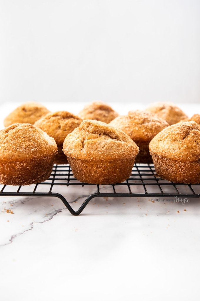 A batch of cinnamon sugar muffins on a black cooling rack on a marble surface