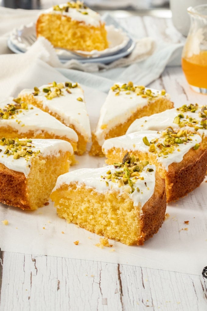 Greek Orange Semolina Cake sliced up, sitting on a piece of baking paper, one slice is on a plate in the background.