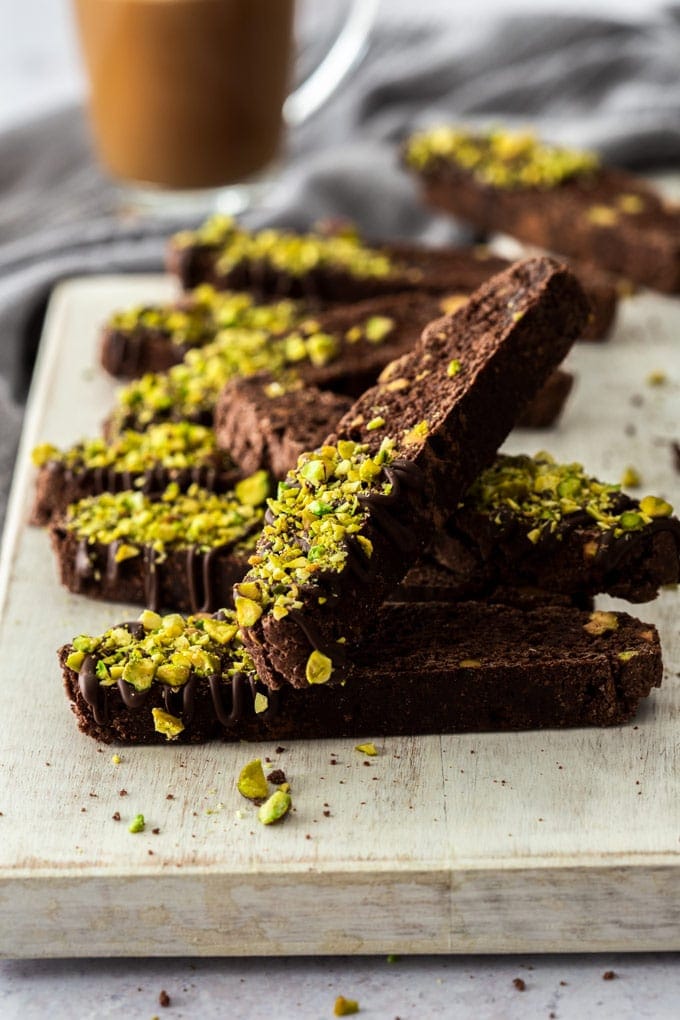 Pieces of chocolate biscotti sprinkled with pistachios, piled up on a white board