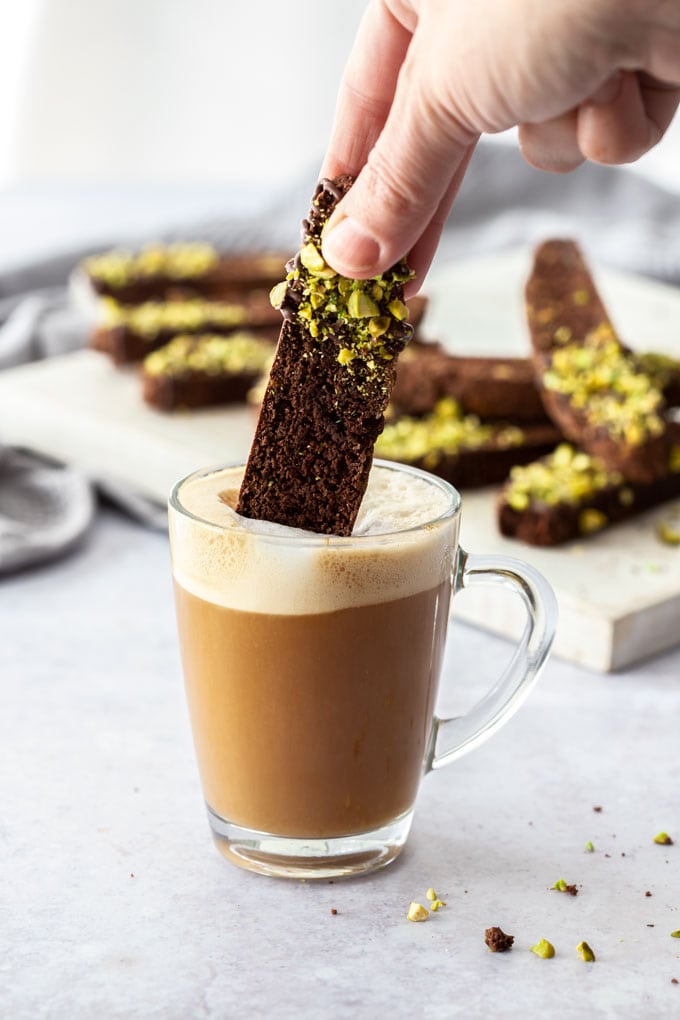 A piece of chocolate biscotti being dunked into a glass cup of coffee
