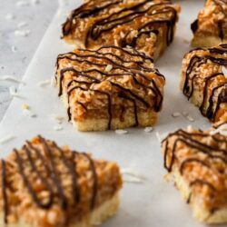 A group of caramel coconut bars, drizzled with chocolate on a piece of baking paper
