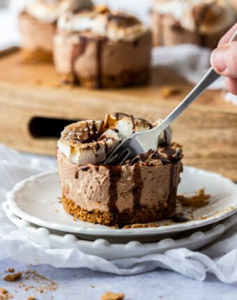 A fork digging into a mini cheesecake on a white plate with a wooden tray in the background