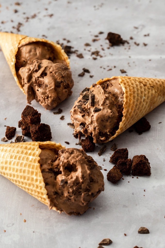 Three waffle cones filled with chocolate ice cream laying on a concrete bench top