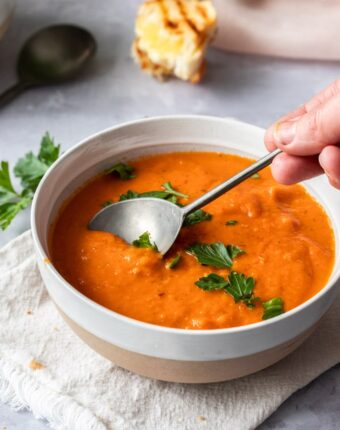 A spoon dipping into a bowl of tomato soup