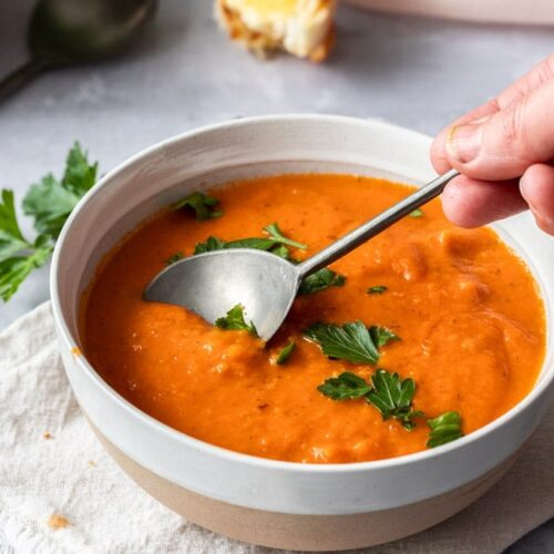 A spoon dipping into a bowl of tomato soup