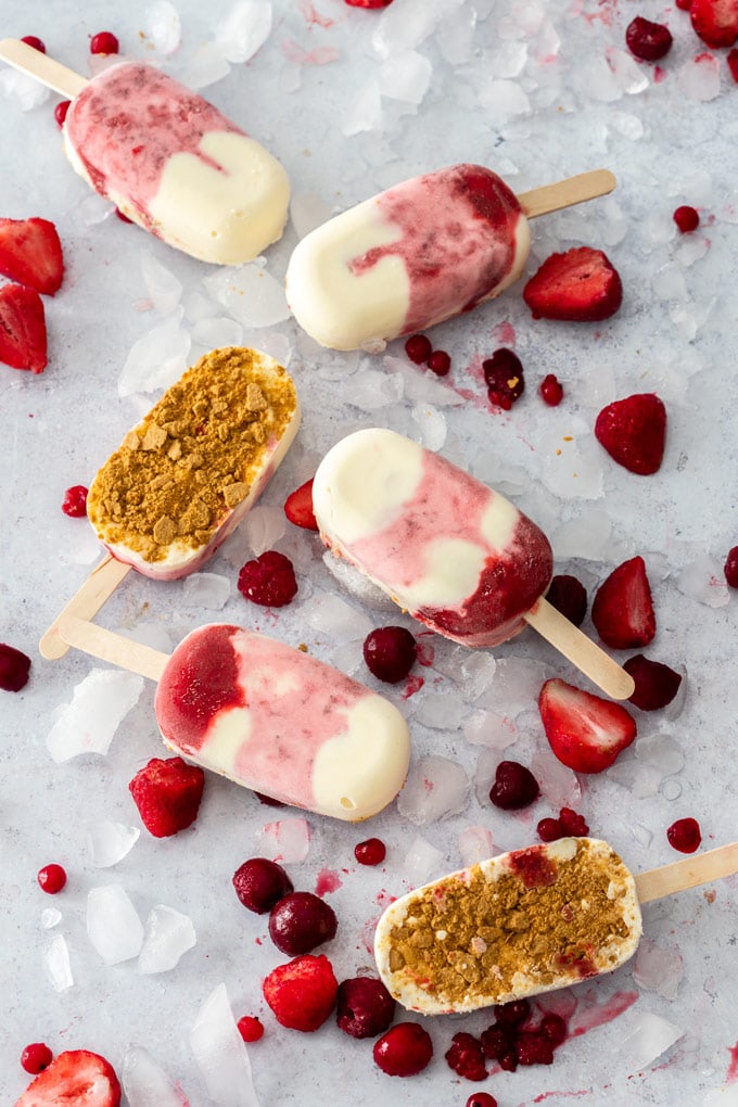 Flatlay of 6 Strawberry Cheesecake Ice Cream Bars on a concrete background surrounded by ice and berries