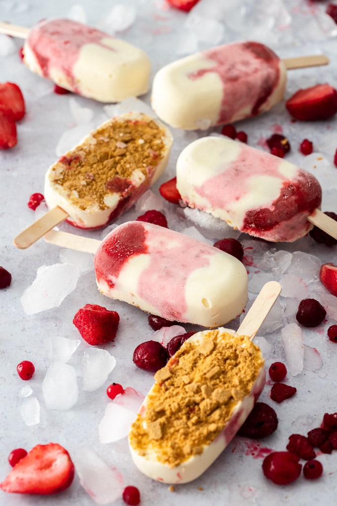 6 Strawberry Cheesecake Ice Cream Bars on a concrete background surrounded by ice and berries