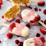 6 Strawberry Cheesecake Ice Cream Bars on a concrete background surrounded by ice and berries
