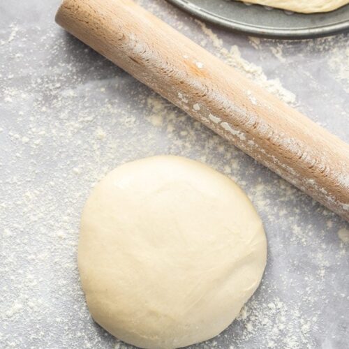 Birdseye view of a ball of pizza dough with a rolling pin next to it