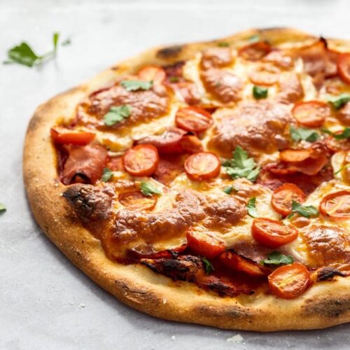 A pizza topped with tomato paste, ham, tomato and mozzarella.