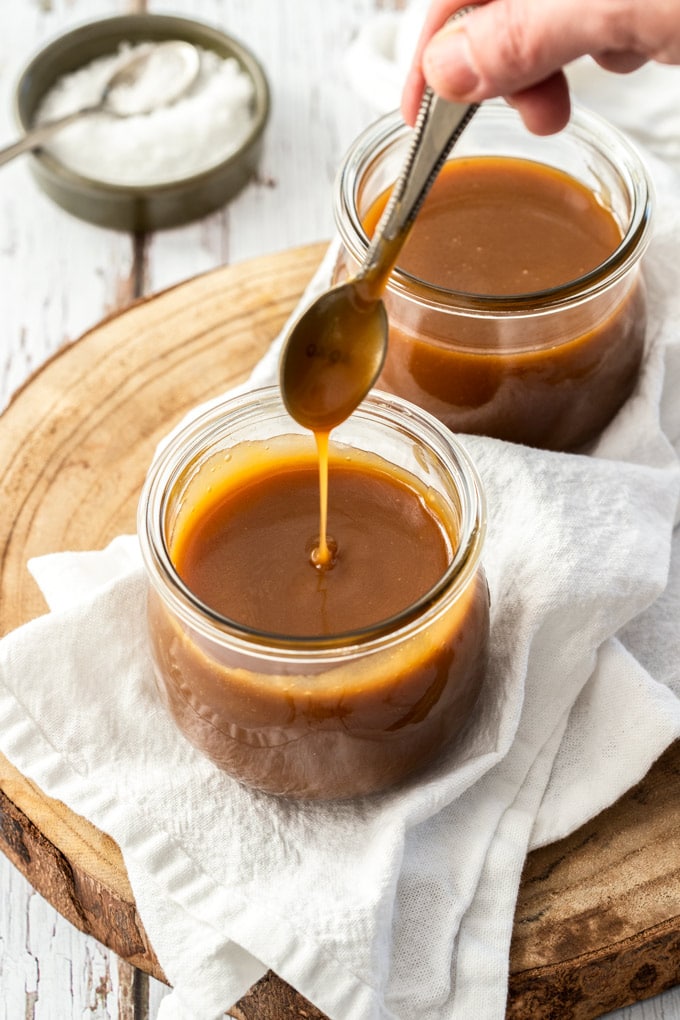 A spoon drizzling caramel sauce into a glass jar.