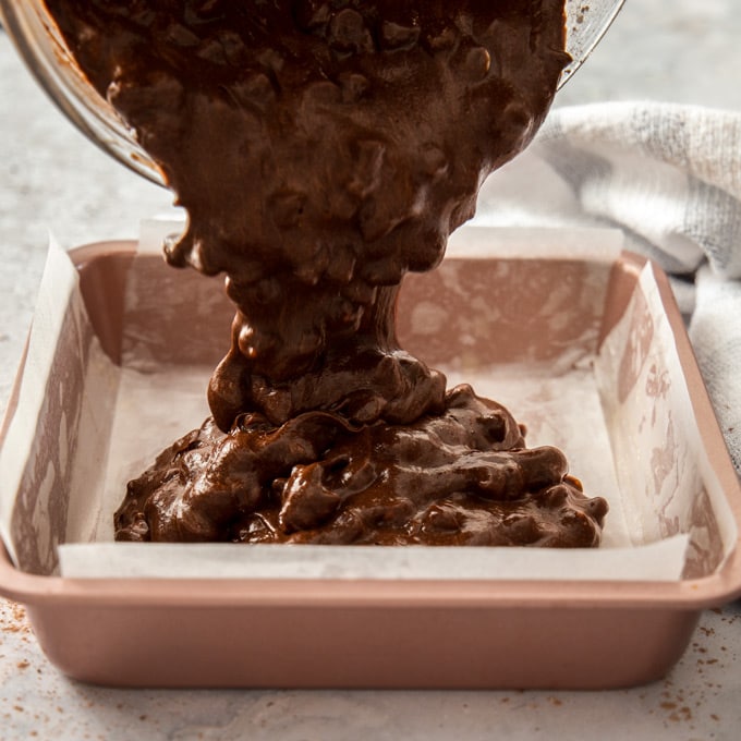 Brownie batter being poured into a lined baking tin