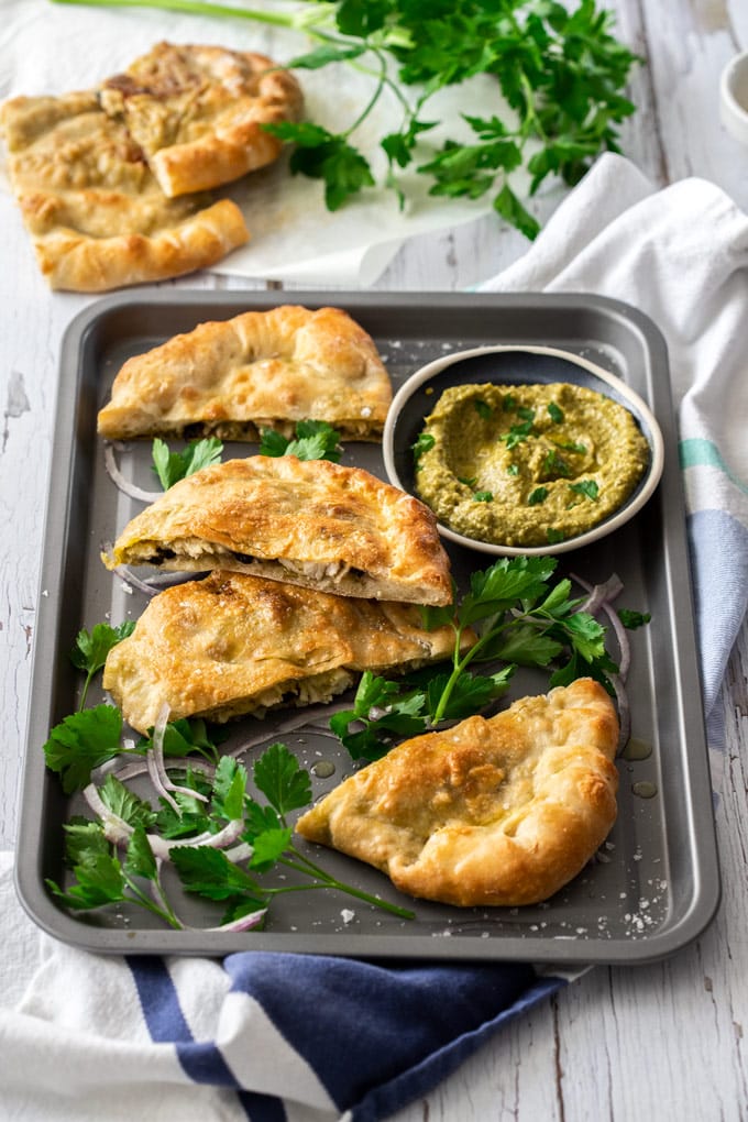 Pesto chicken calzone slices on a grey baking tray surrounded by parsley and onion