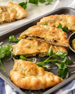 Slices of calzone on a grey baking tray surrounded by parsley and onion.