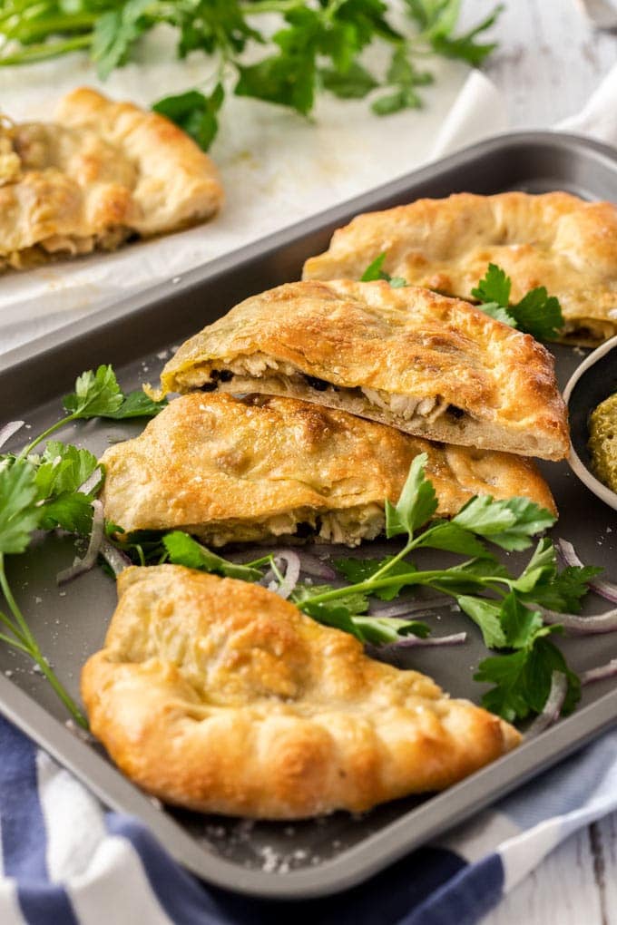 Slices of calzone on a grey baking tray surrounded by parsley and onion.
