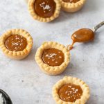 6 caramel cookie cups on a concrete background with a spoon filled with caramel next to them.