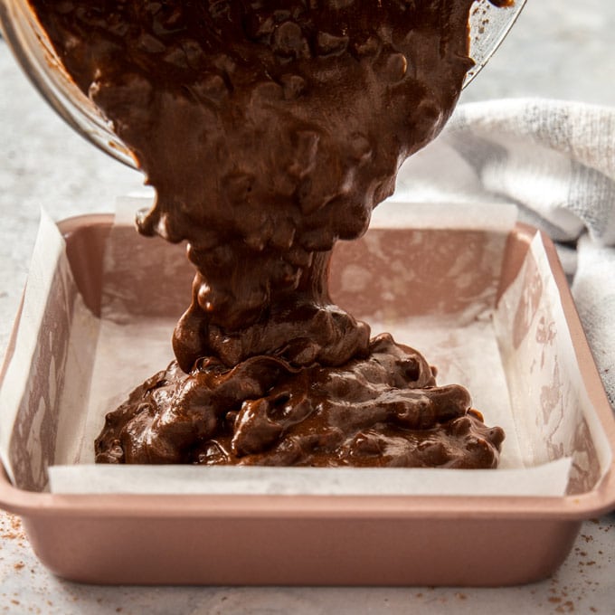 Pouring chocolate chip brownie batter into a pink baking tin.
