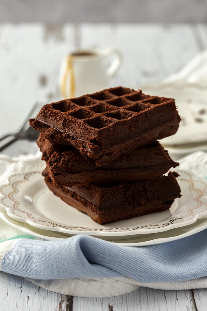 A stack of 3 waffle brownies on a white plate on top of a blue tea towel