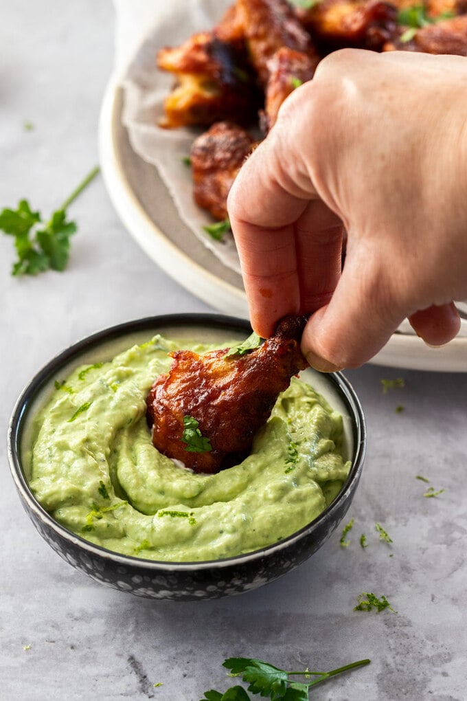 A chicken wing being dipped into avocado cream sauce