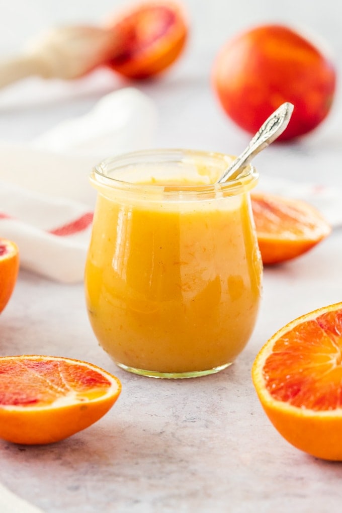A glass jar filled with orange curd with a spoon sticking out.