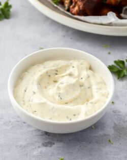 A small white bowl filled with ranch dip on a concrete surface.