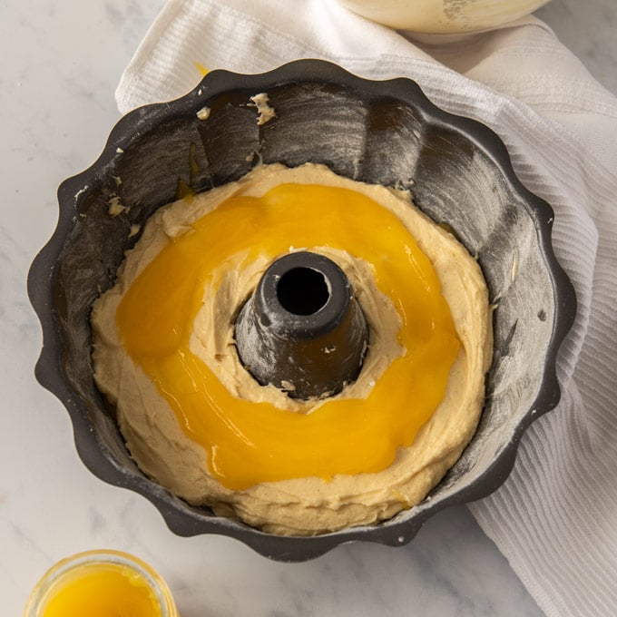 A bundt tin with a layer of cake batter, topped with a layer of lemon curd