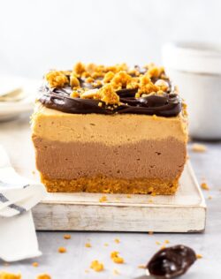 Front on view of the inside of a square slice of peanut butter cheesecake. it sits on a white board with a spoon of ganache in front