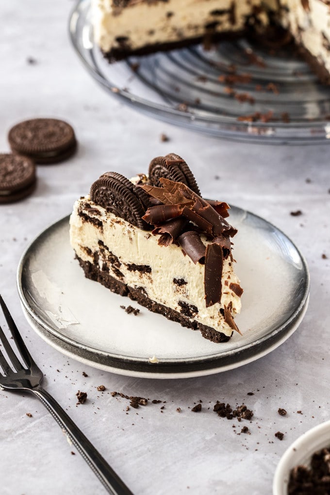 A slice of cheesecake on a white plate with oreos and crumbs strewn around. 
